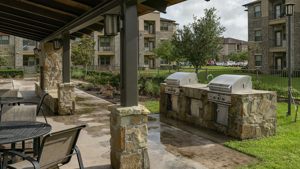 an outdoor kitchen with two grills and a patio with a table and chairs