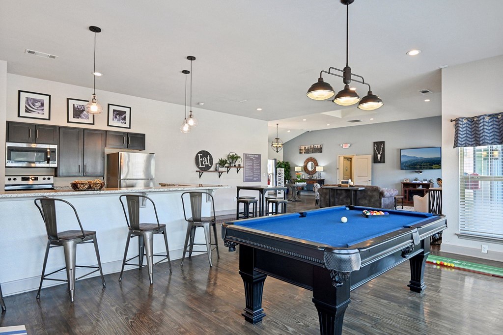 a pool table in a living room with a bar and a kitchen