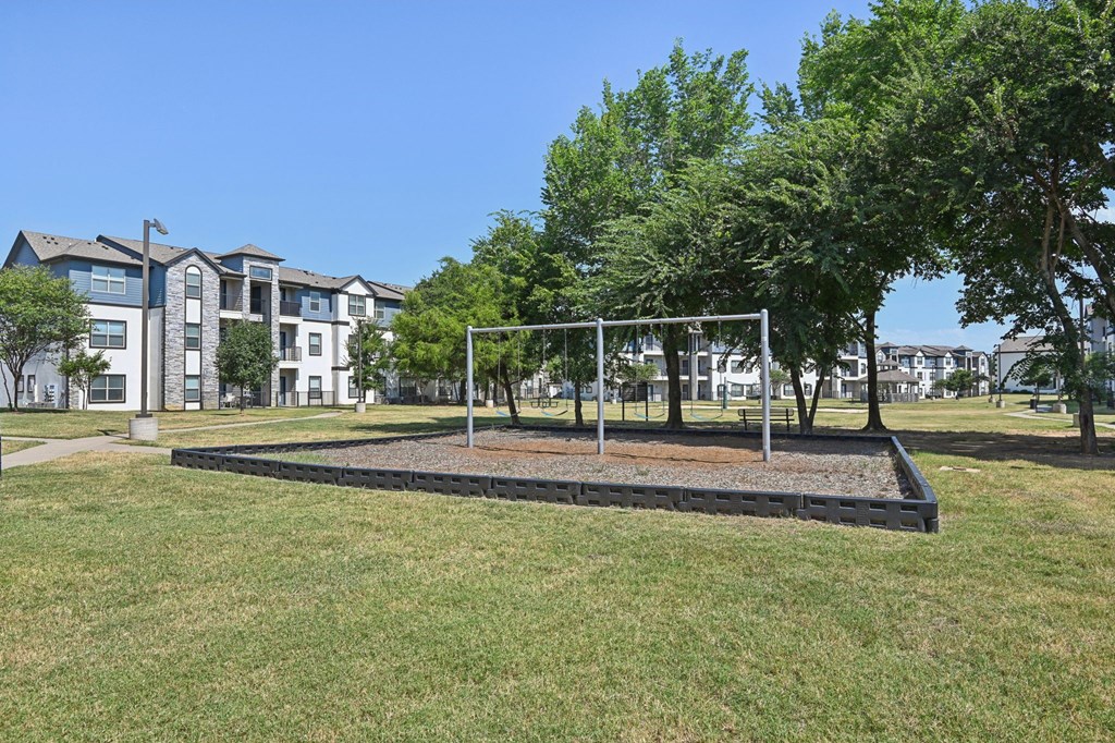 a park with a swing set and trees in front of an apartment building