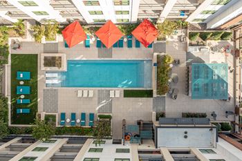 A swimming pool is surrounded by a patio with chairs and umbrellas.