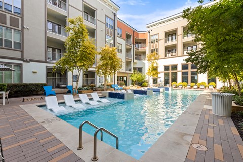 A pool surrounded by chairs and trees in front of apartment buildings.