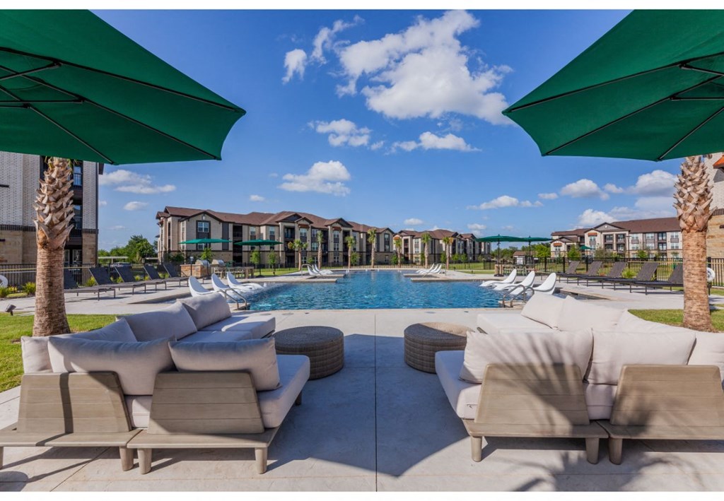 a swimming pool with lounge chairs and umbrellas and apartments in the background