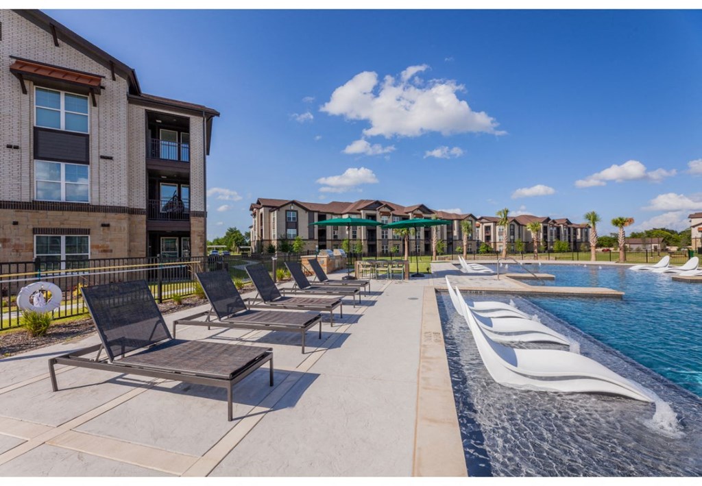 a pool with lounge chairs and umbrellas in front of apartment buildings