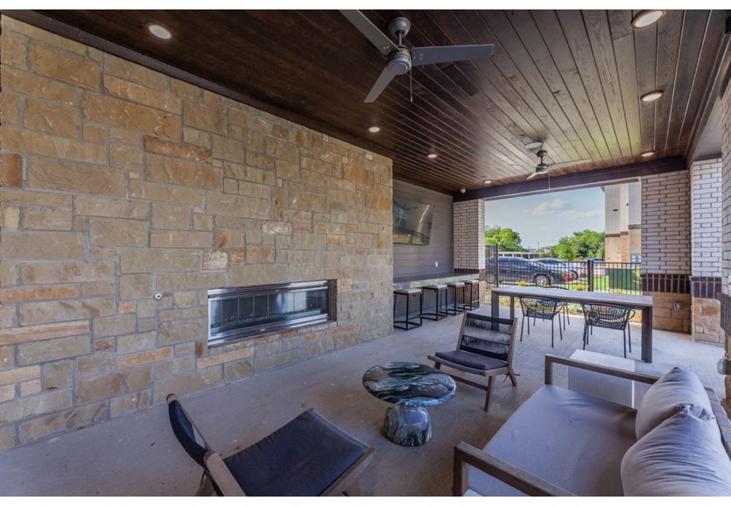 a covered patio with a stone wall and a fireplace
