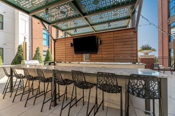A patio with a bar and chairs under a glass roof.