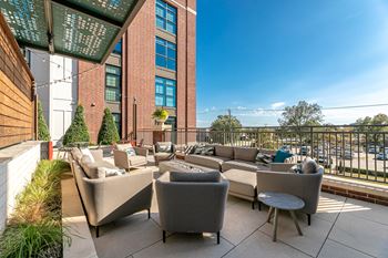 A patio with grey couches and a table with a glass roof.