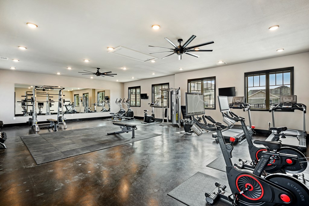 a spacious fitness room with cardio equipment and windows