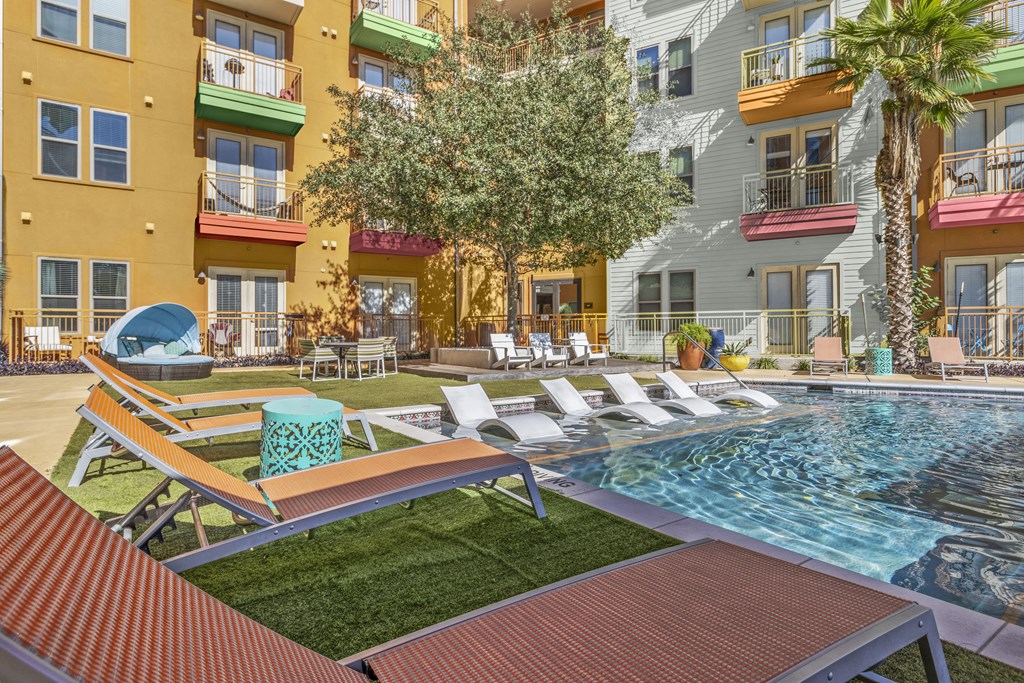 a pool with lounge chairs and a tree in front of a building
