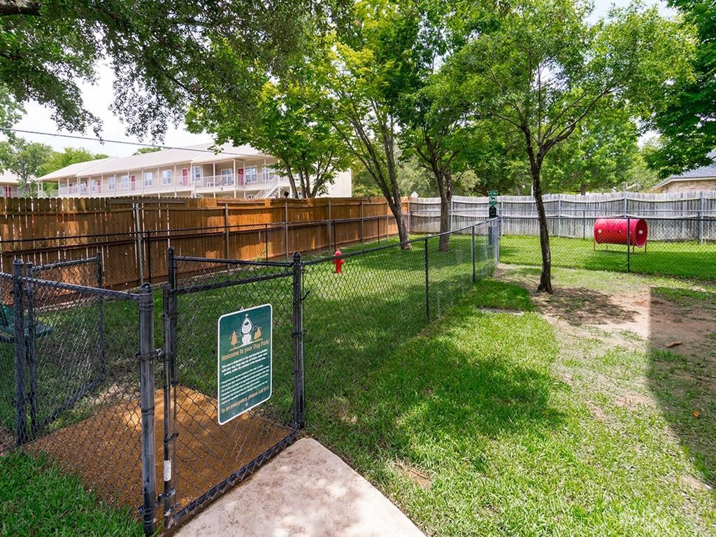 a dog park in a fenced in area with trees and a sign