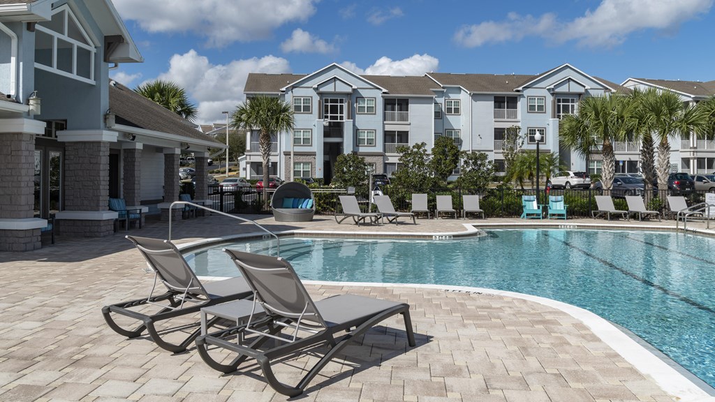 a swimming pool with chaise lounge chairs and a resort style building in the background