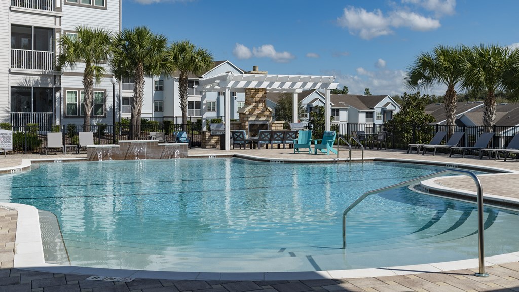 a large swimming pool with blue chairs and a white pergola in the background