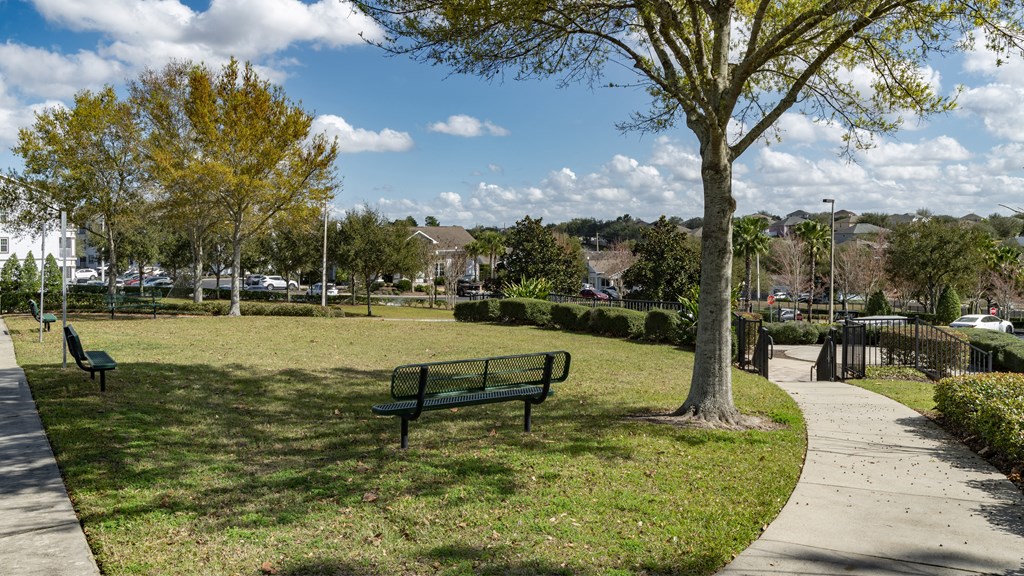 a park bench in a grassy area with trees and houses in the background