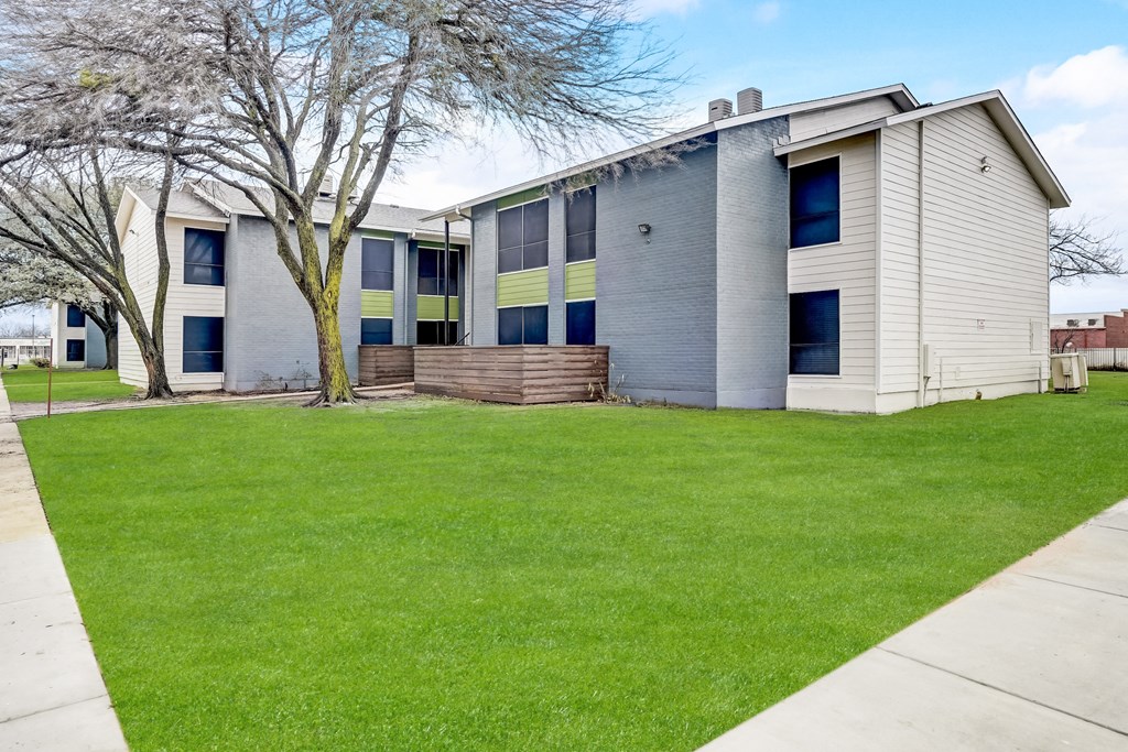 a gray and white building with a green lawn in front of it