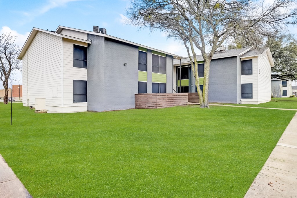 a white and gray building with a green lawn in front of it