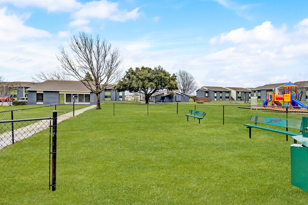 a fenced in grassy area with a playground and houses in the background