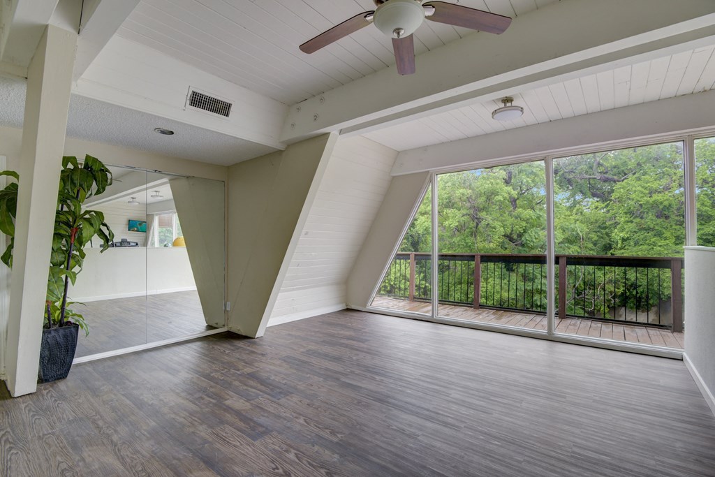 an empty living room with a ceiling fan and large windows