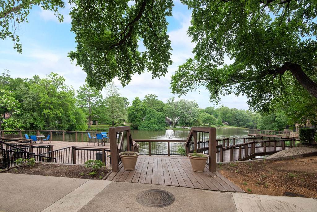 a deck overlooking a body of water with trees and a fountain