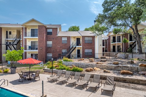 A pool area with chairs and a red umbrella in front of apartment buildings.