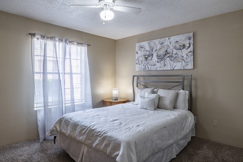 A bedroom with a bed, pillows, a ceiling fan, and a painting on the wall.