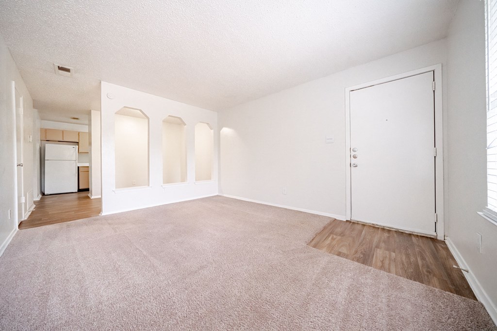 an empty living room with a door to a kitchen