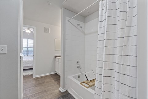A white bathroom with a shower curtain and a wooden tray on the tub.