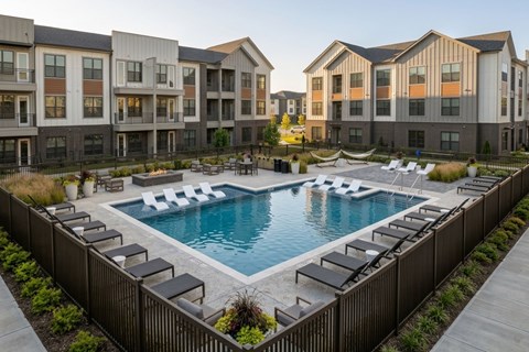 A swimming pool surrounded by lounge chairs in front of apartment buildings.