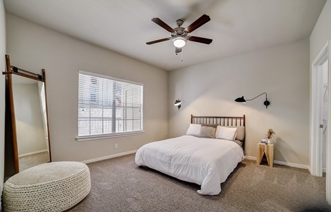 A bedroom with a bed, a ceiling fan, and a window with blinds.