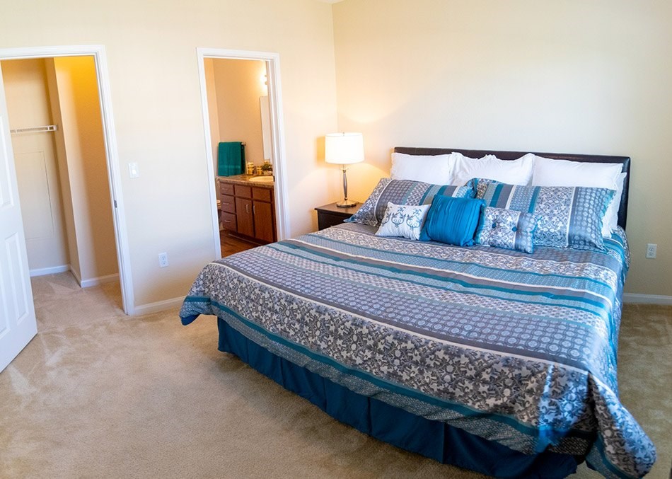 A bed with a blue comforter and pillows is in a room with a carpeted floor.