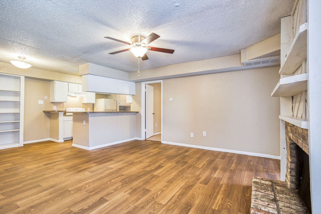 an empty living room with a ceiling fan and a kitchen