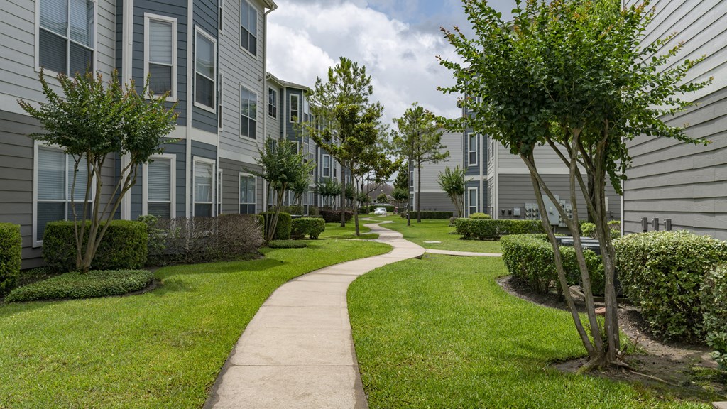 a walkway between two apartment buildings with grass and trees