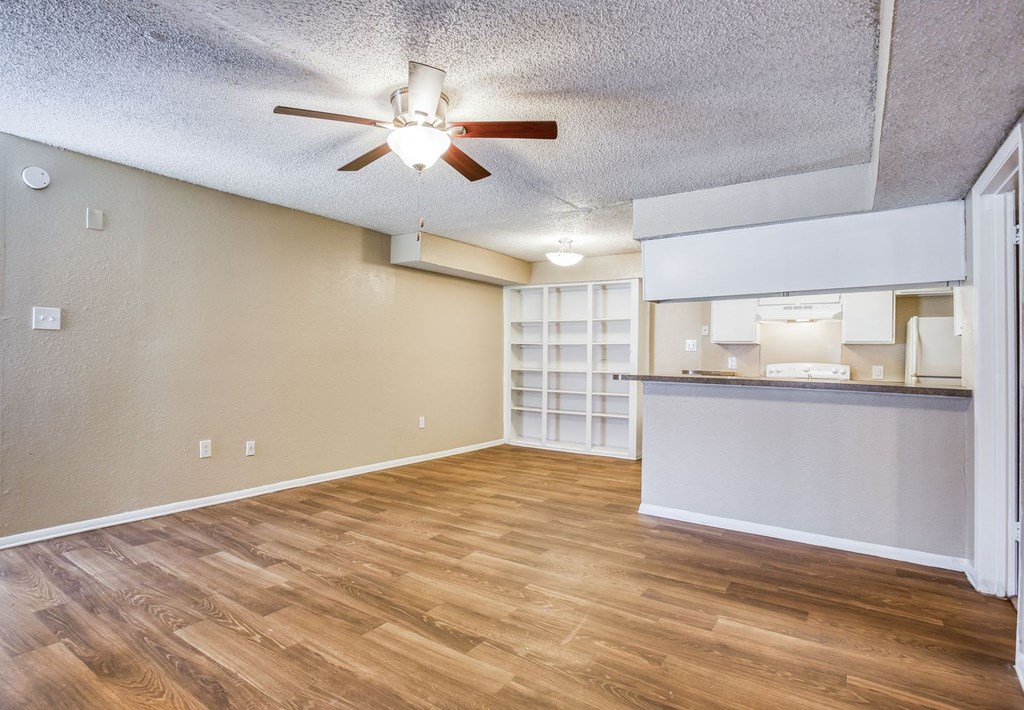 an empty living room with a ceiling fan and a kitchen