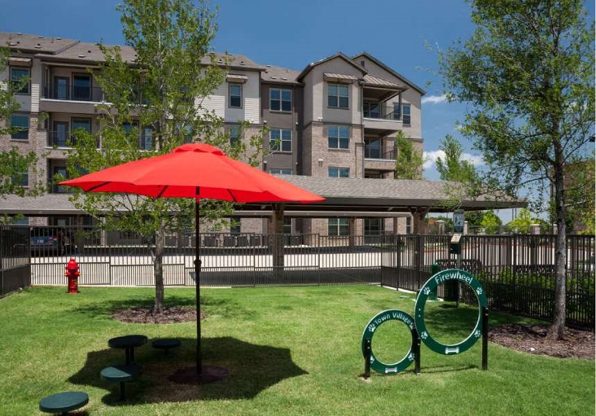 a park with a red umbrella in front of an apartment building