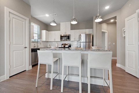 an open kitchen with white cabinets and a bar with white chairs