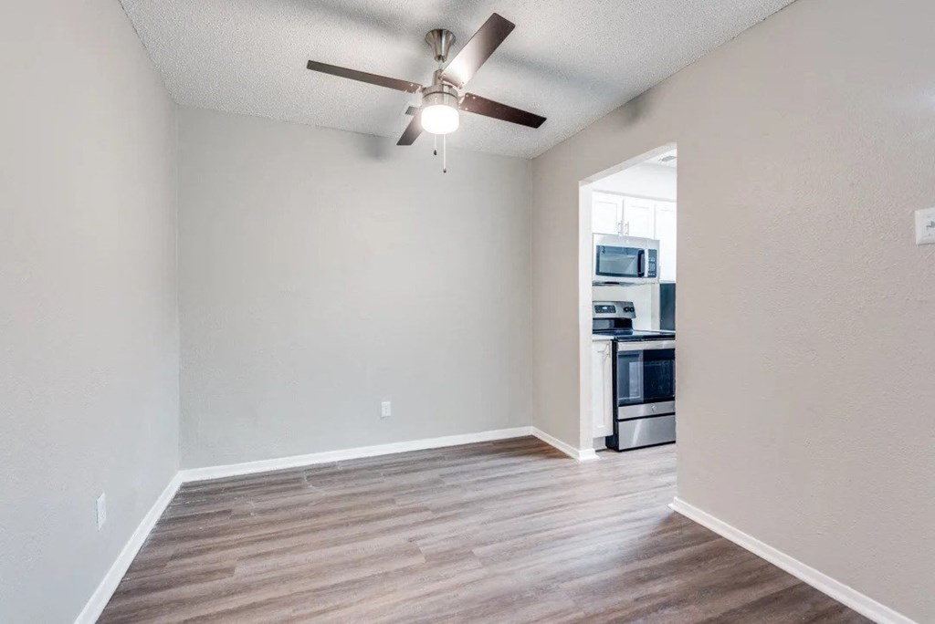 an empty living room with a ceiling fan and a kitchen