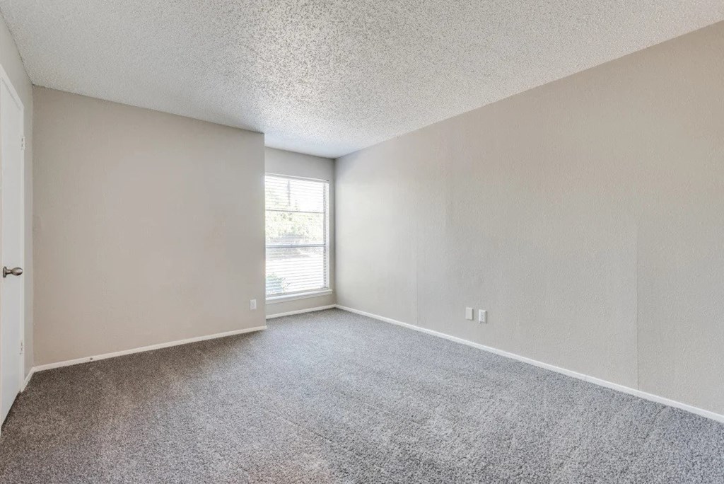 an empty living room with a window and carpeting