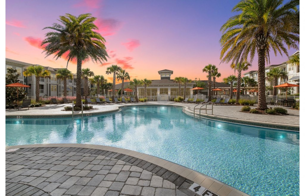 a large swimming pool with palm trees and a building in the background