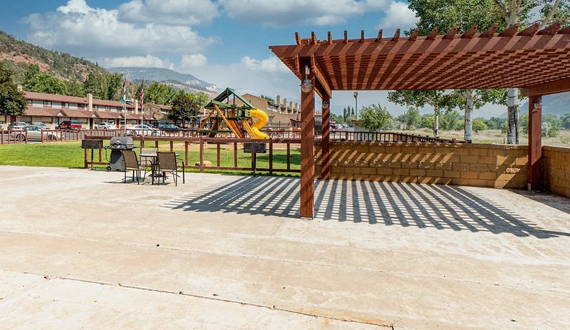 a patio with a pergola and a playground in the background
