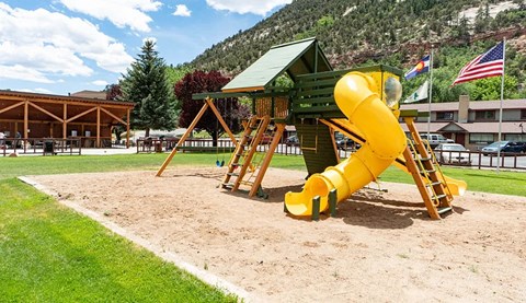 a yellow slide in a playground with a picnic shelter in the background