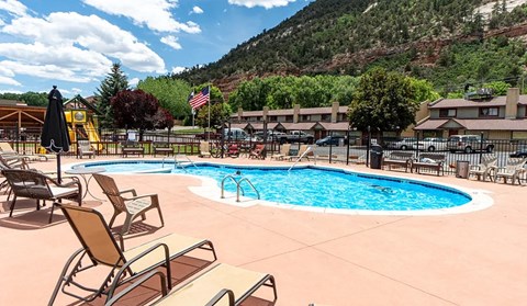 a pool with lounge chairs and a slide at the foot of a mountain
