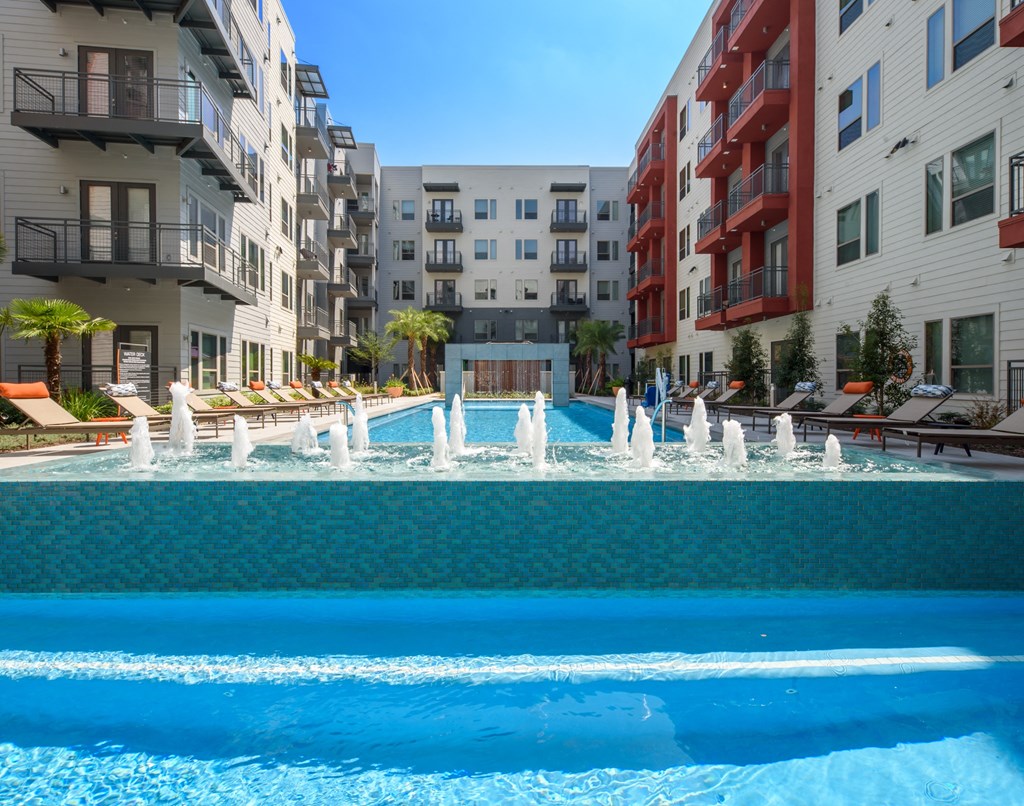 a large pool with water jets in front of apartment buildings