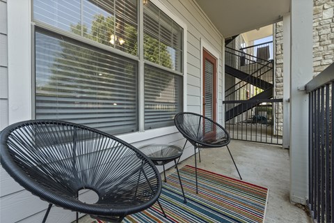 A black metal chair and table are on a porch with a striped rug.