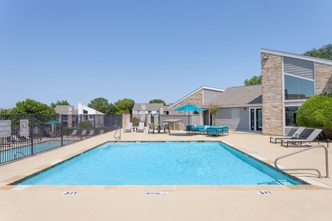 Swimming pool with sundeck, grilling station, and umbrella-shaded lounge seating beside the clubhouse.