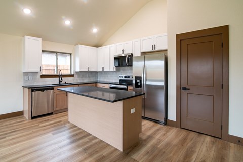 A kitchen with a stainless steel refrigerator and wooden floors.