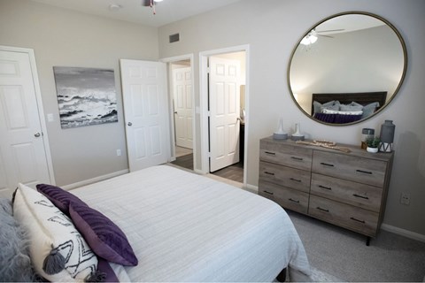 A bedroom with a round mirror and a bed with a purple pillow.