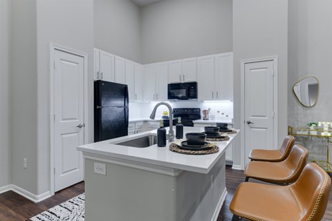 A kitchen with a black refrigerator, white cabinets, and a white island with brown chairs.