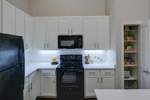 A black refrigerator stands in a kitchen with white cabinets and a black stove.