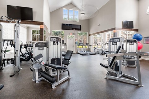 Spacious fitness center with strength machines, cardio equipment, vaulted ceilings, and large windows.