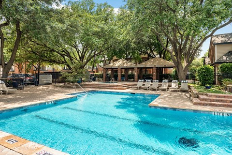 Outdoor swimming pool with shaded cabanas, sun loungers, and mature trees.