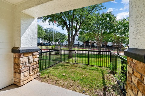 Covered patio with stone columns and fenced grassy yard at Villas of Vista Ridge.