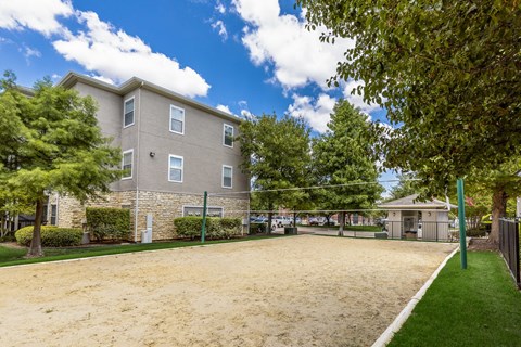 A large sandy area in front of a building with trees on the left.